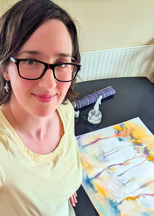 The artist in her studio with an unfinished painting on the table next to her