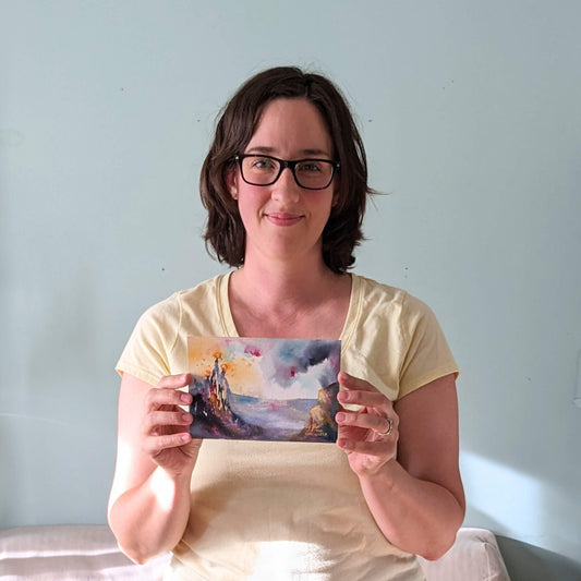 Woman holding a painting of burning trees over a colorful landscape in front of a light blue wall