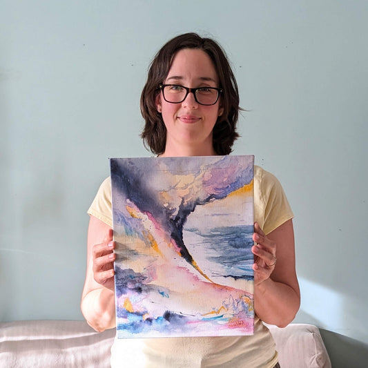 Person holding a colorful abstract painting against a light blue wall.