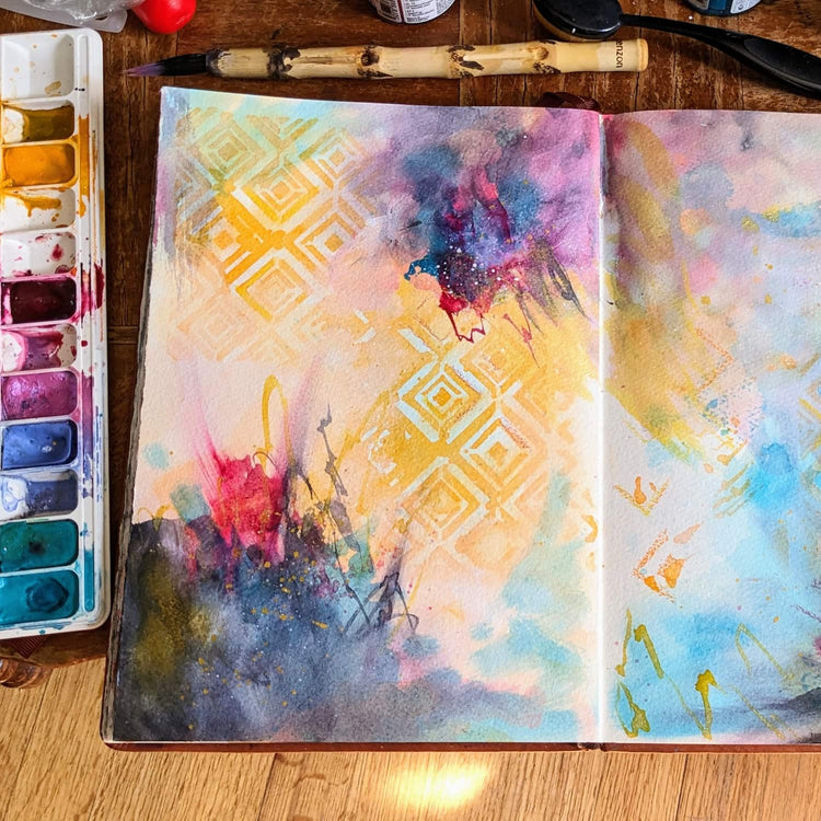 A colorful abstract sketchbook spread open with paint and paintbrush together