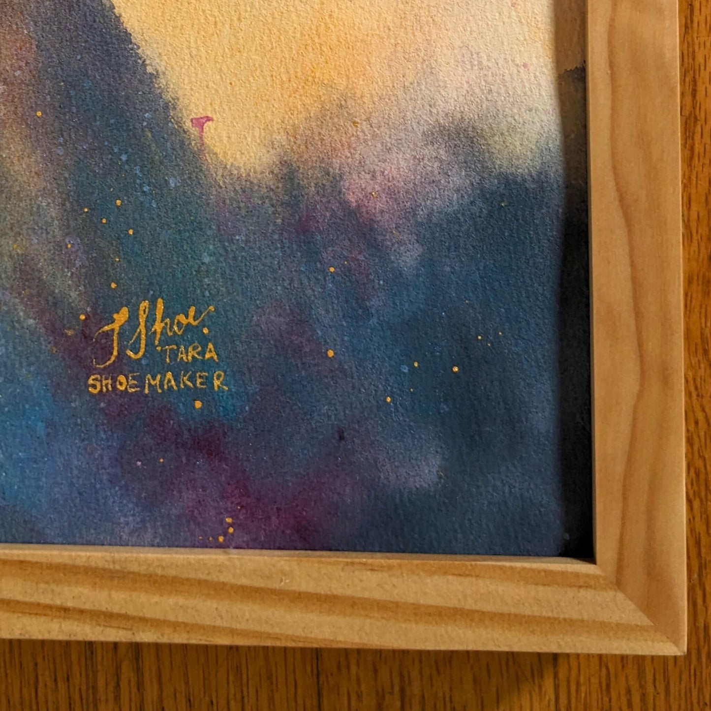Framed abstract painting with gold signature on a wooden surface