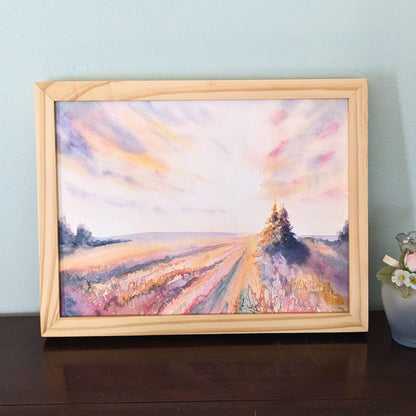 Framed painting of dawn over a field with a tree on a wooden surface.