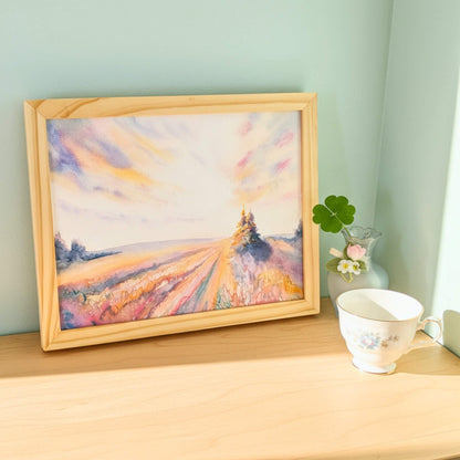 Framed painting of a landscape on a wooden surface with a cup and vase.