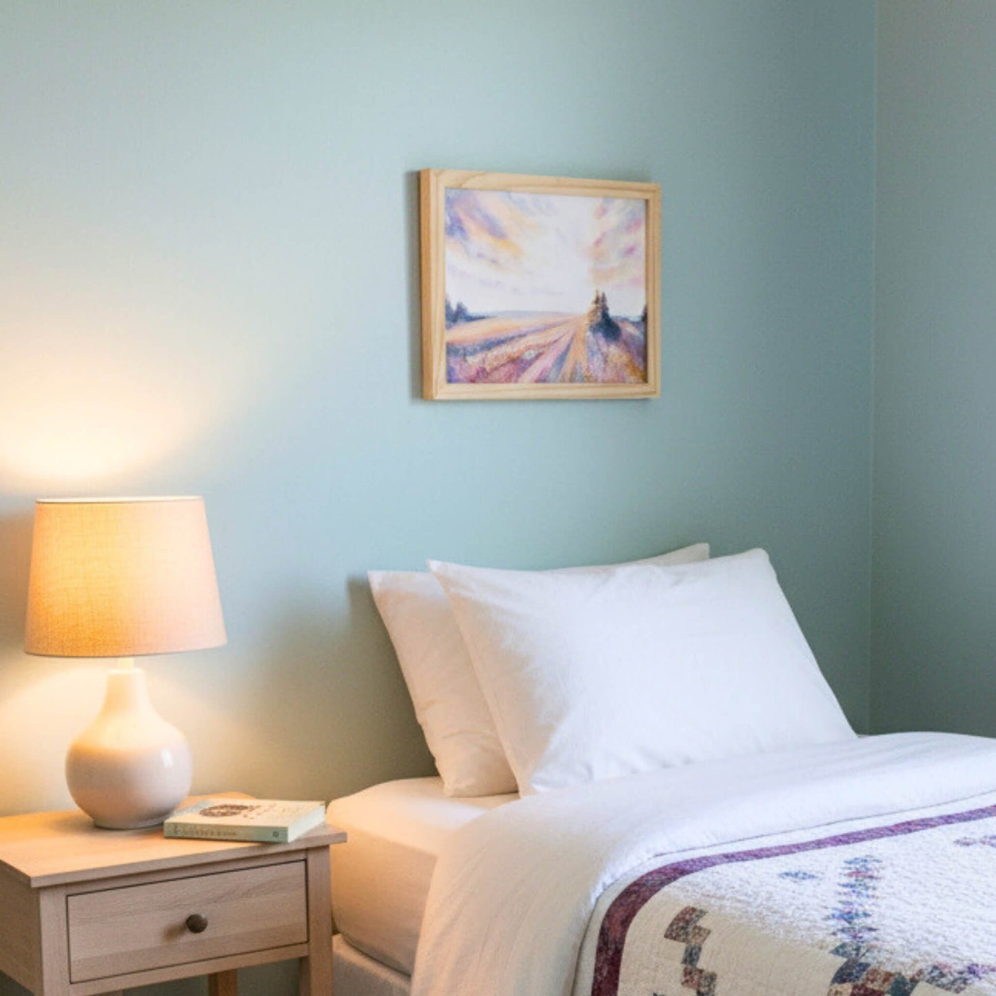 Bedroom with a lamp on a nightstand and a painting on the wall.