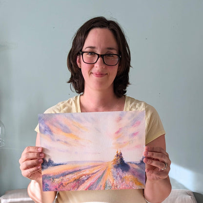 Woman holding a painting of a landscape with a light blue background