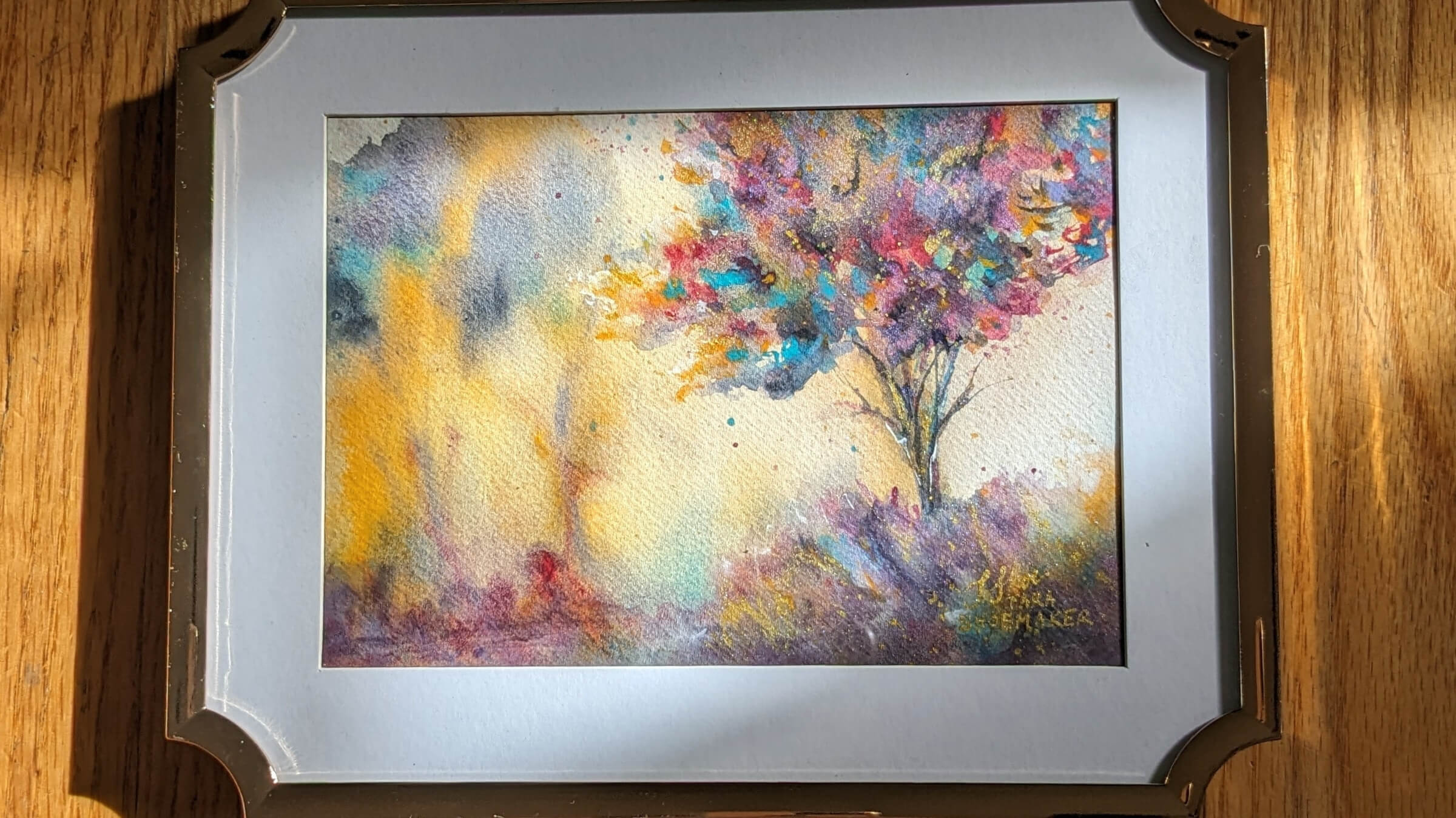Framed abstract painting with a tree on a wooden surface