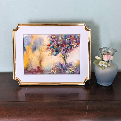 Framed abstract painting on a wooden surface with a small vase and flowers.