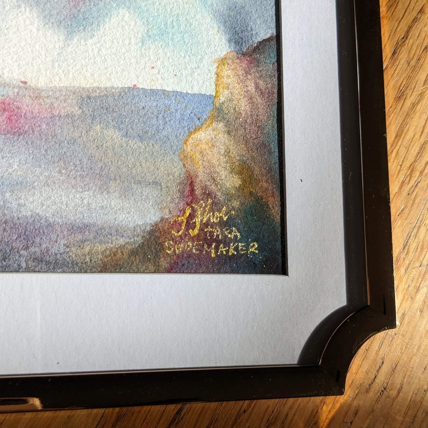 Framed artwork with a colorful landscape and signature on a wooden surface