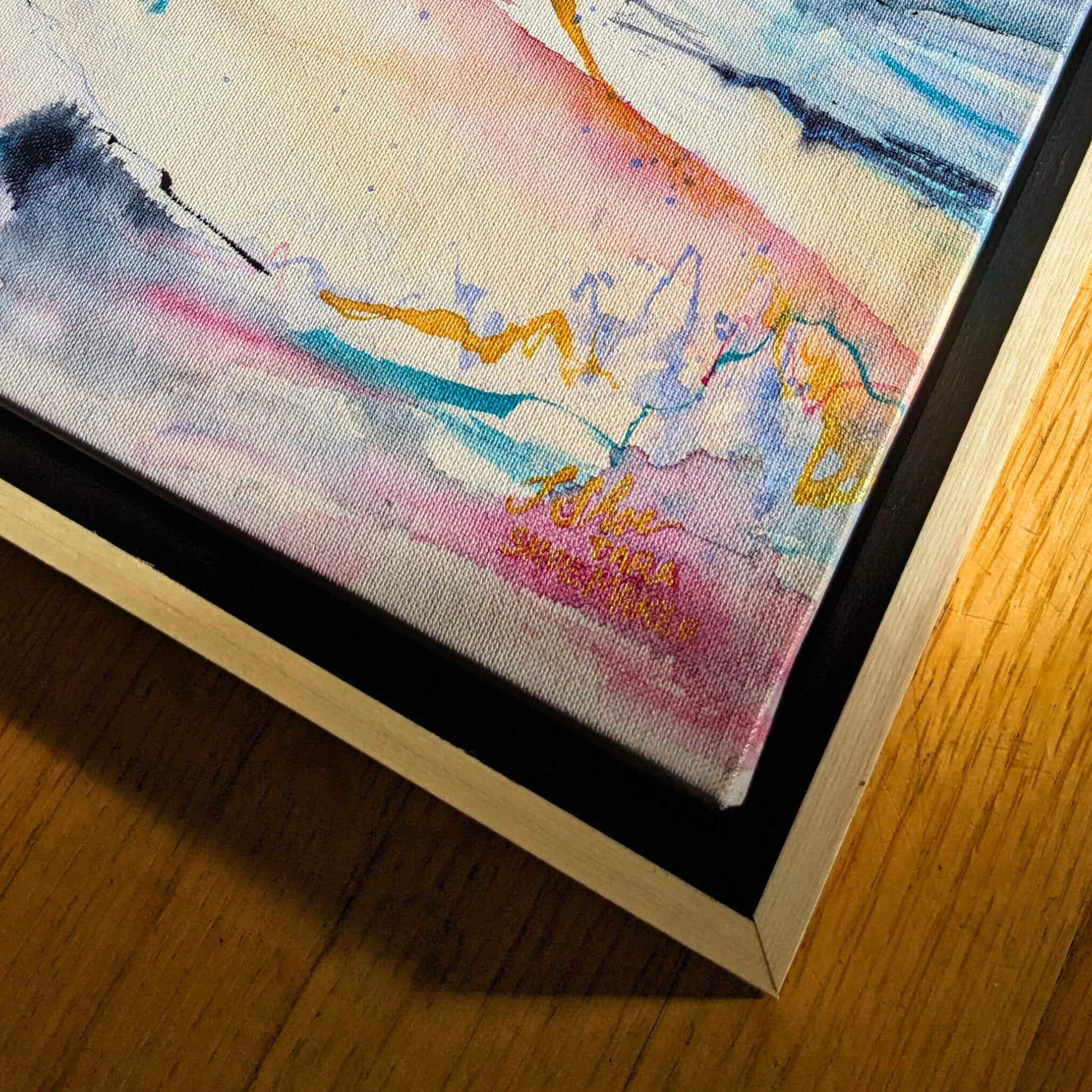 Close-up of a colorful abstract painting with a signature on a wooden surface