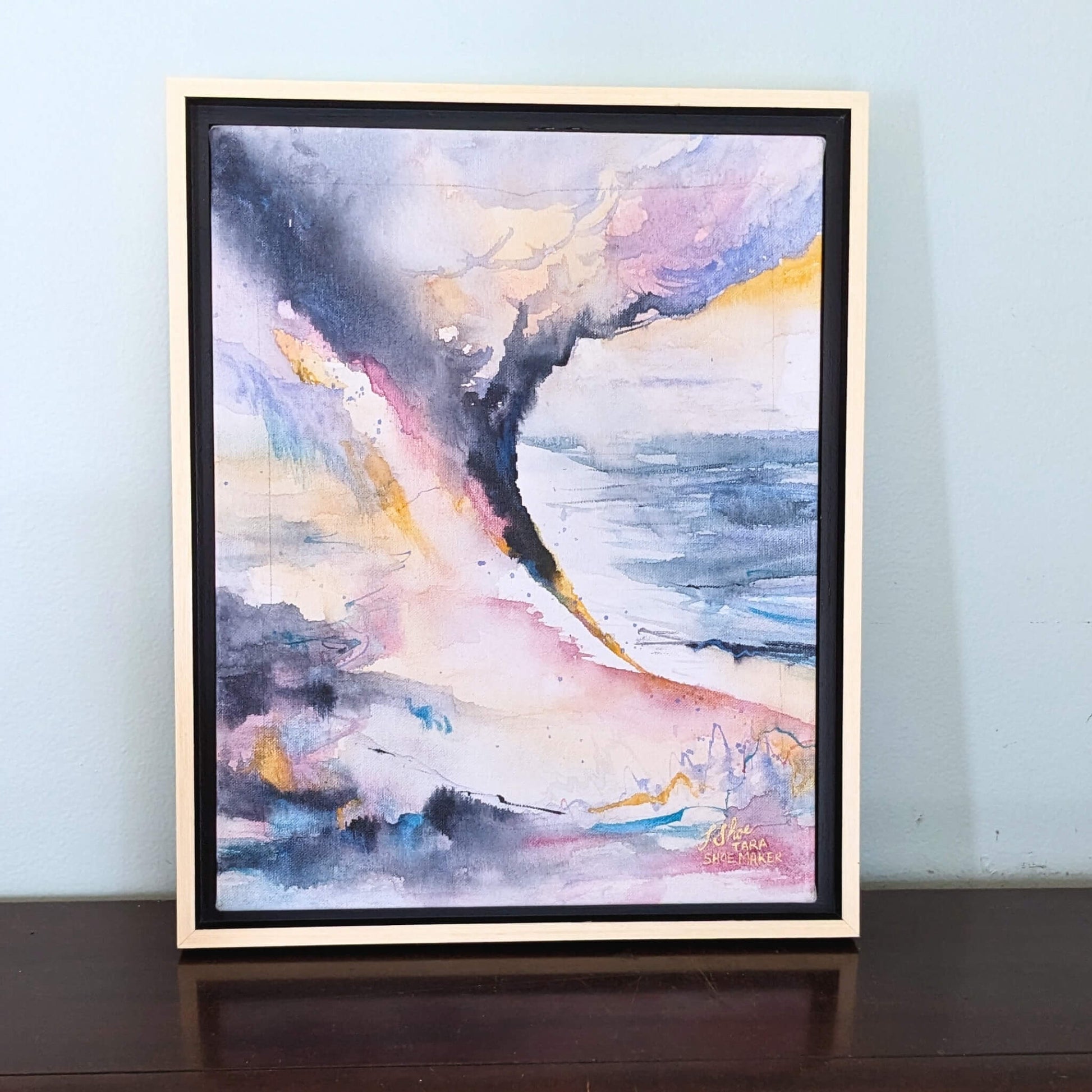 Framed abstract painting with colorful brushstrokes on a light blue wall.