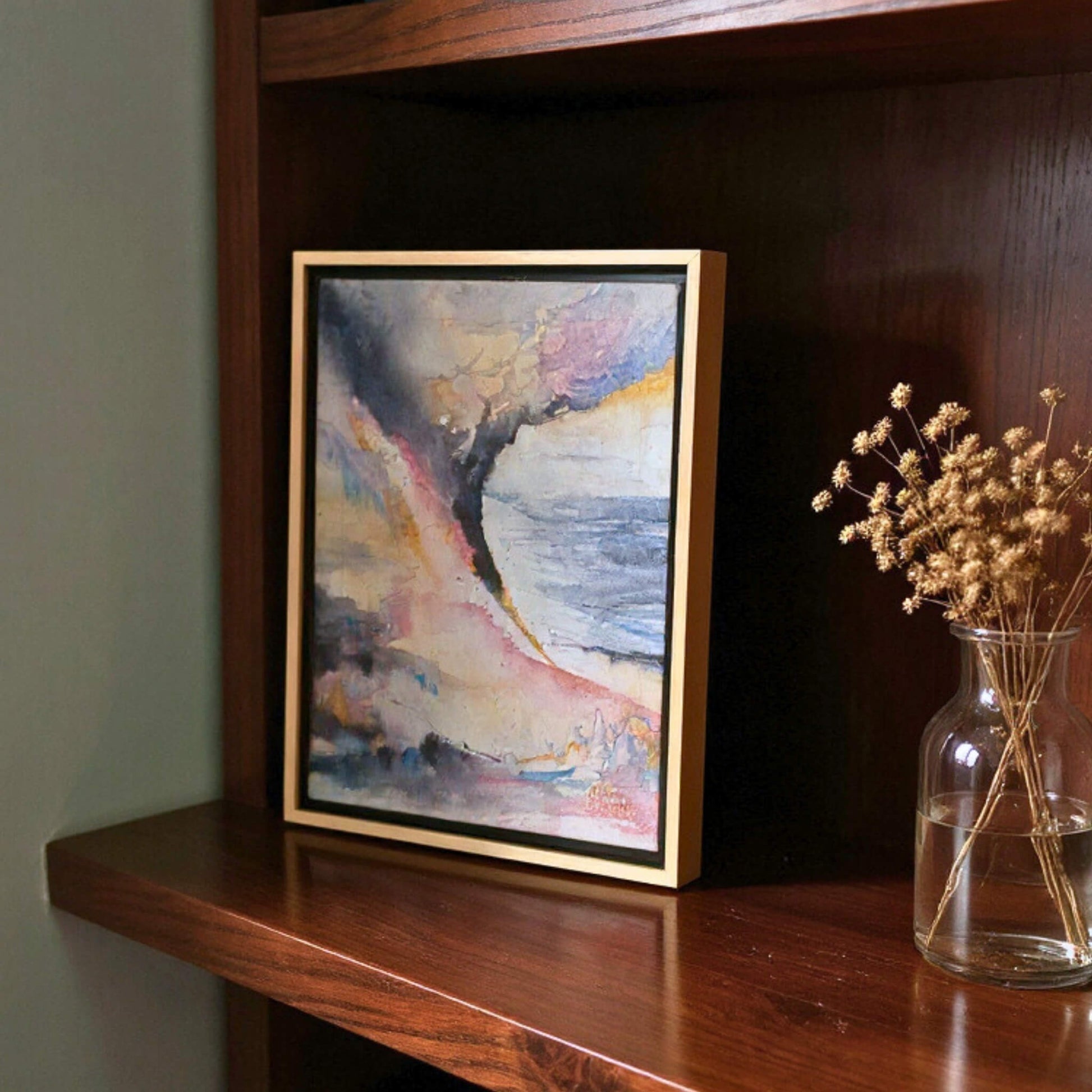 Framed abstract painting on a wooden shelf with a vase of dried flowers.
