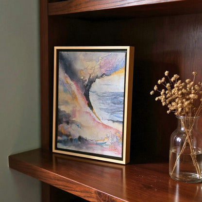 Framed abstract painting on a wooden shelf with a vase of dried flowers.