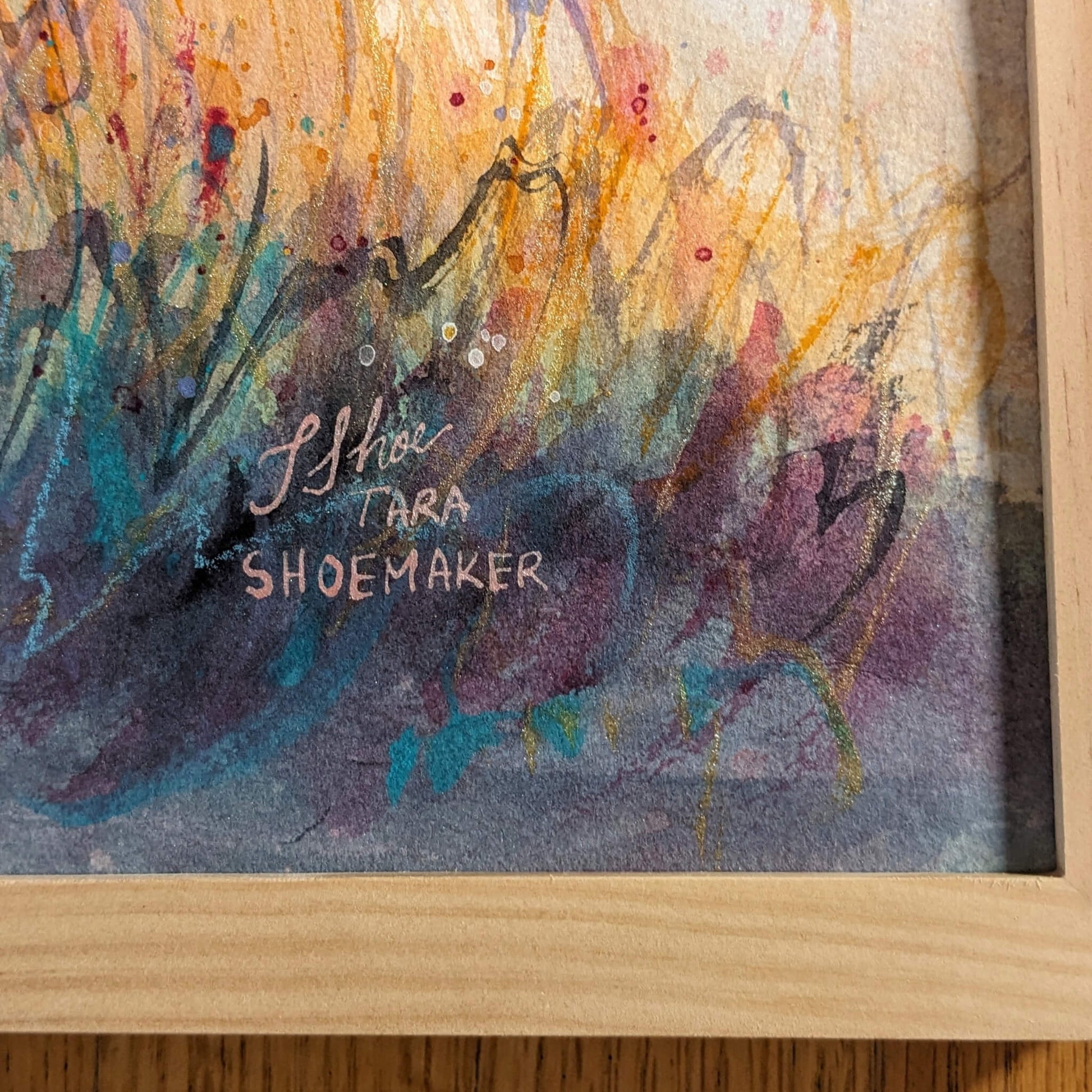 Artistic signature on a colorful abstract painting with a wooden frame.