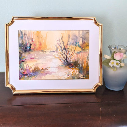 Framed abstract painting on a wooden surface with a vase of flowers in the background.