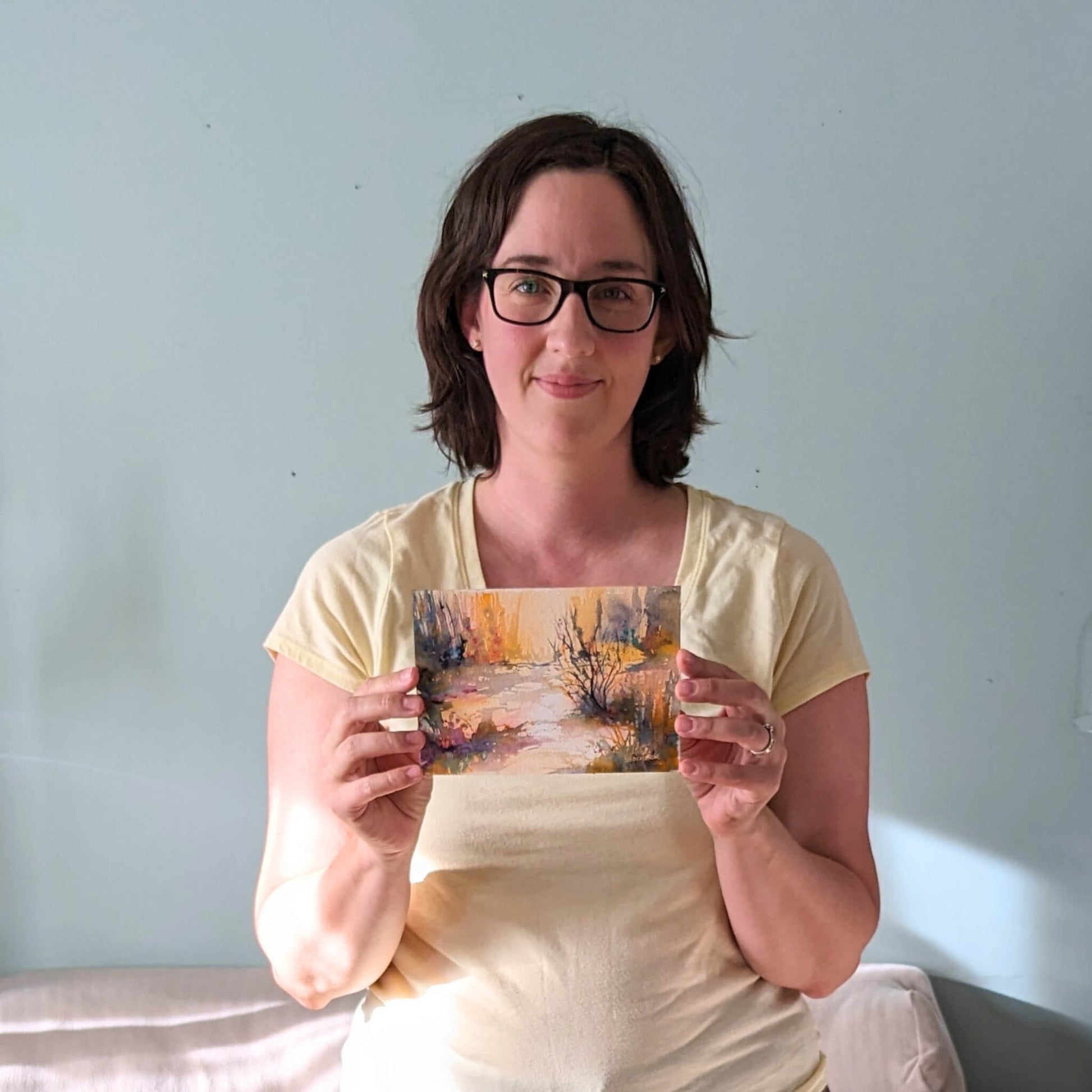 Woman holding a painting against a light blue wall