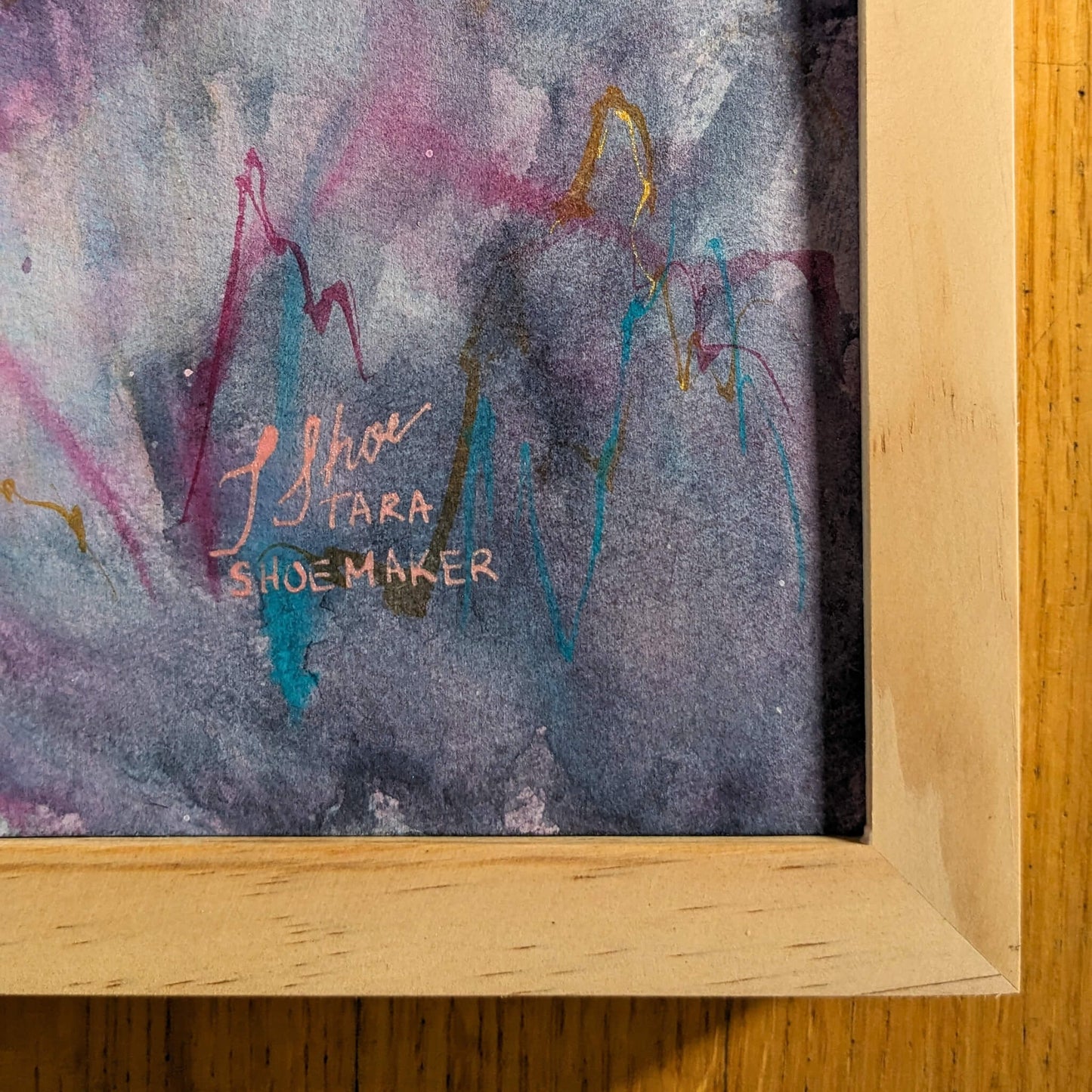Abstract painting with colorful brush strokes and a signature on a wooden surface
