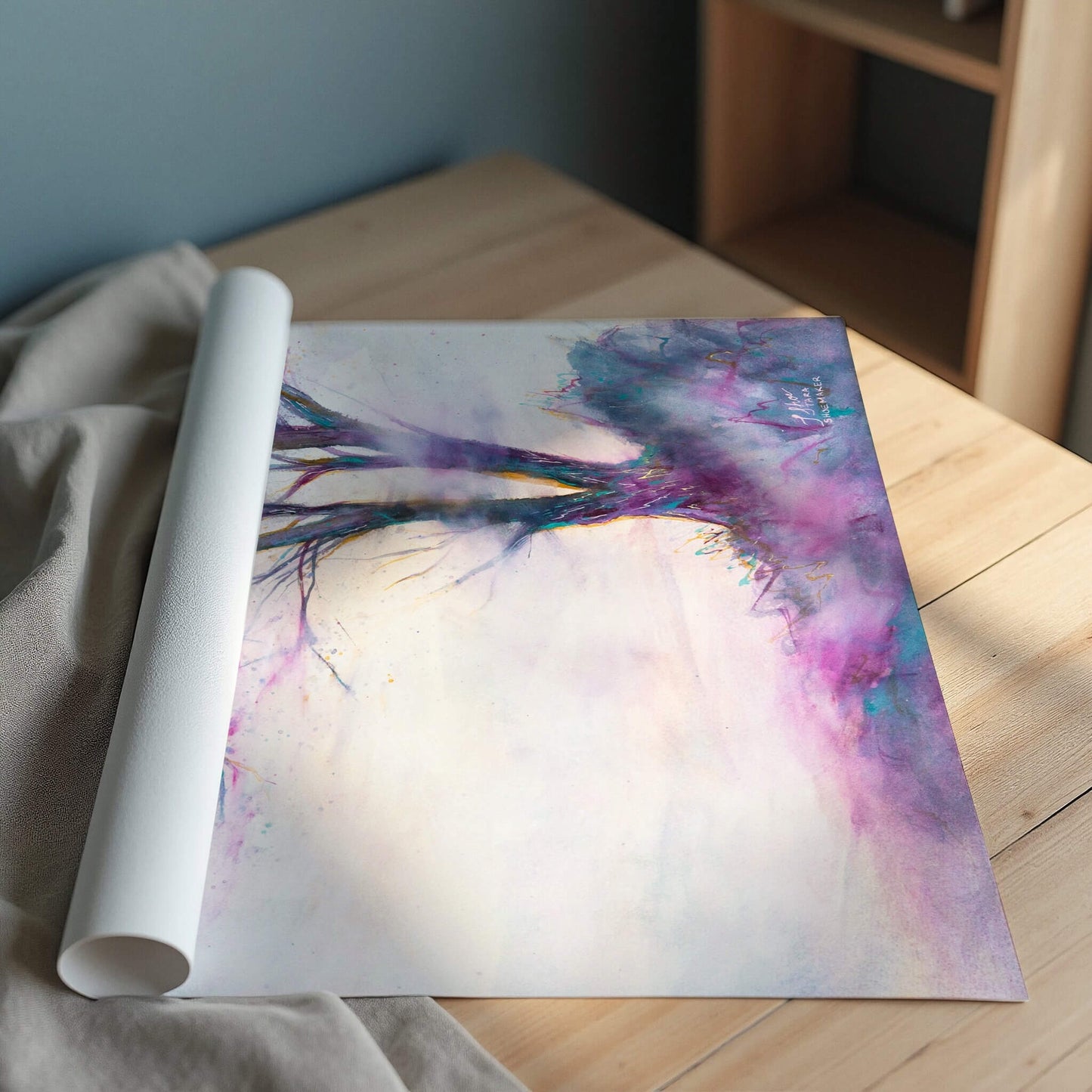 Rolled-up print of abstract artwork with a tree in vibrant colors on a wooden surface