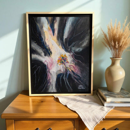 Framed abstract painting on a wooden surface with a vase and books in the background.