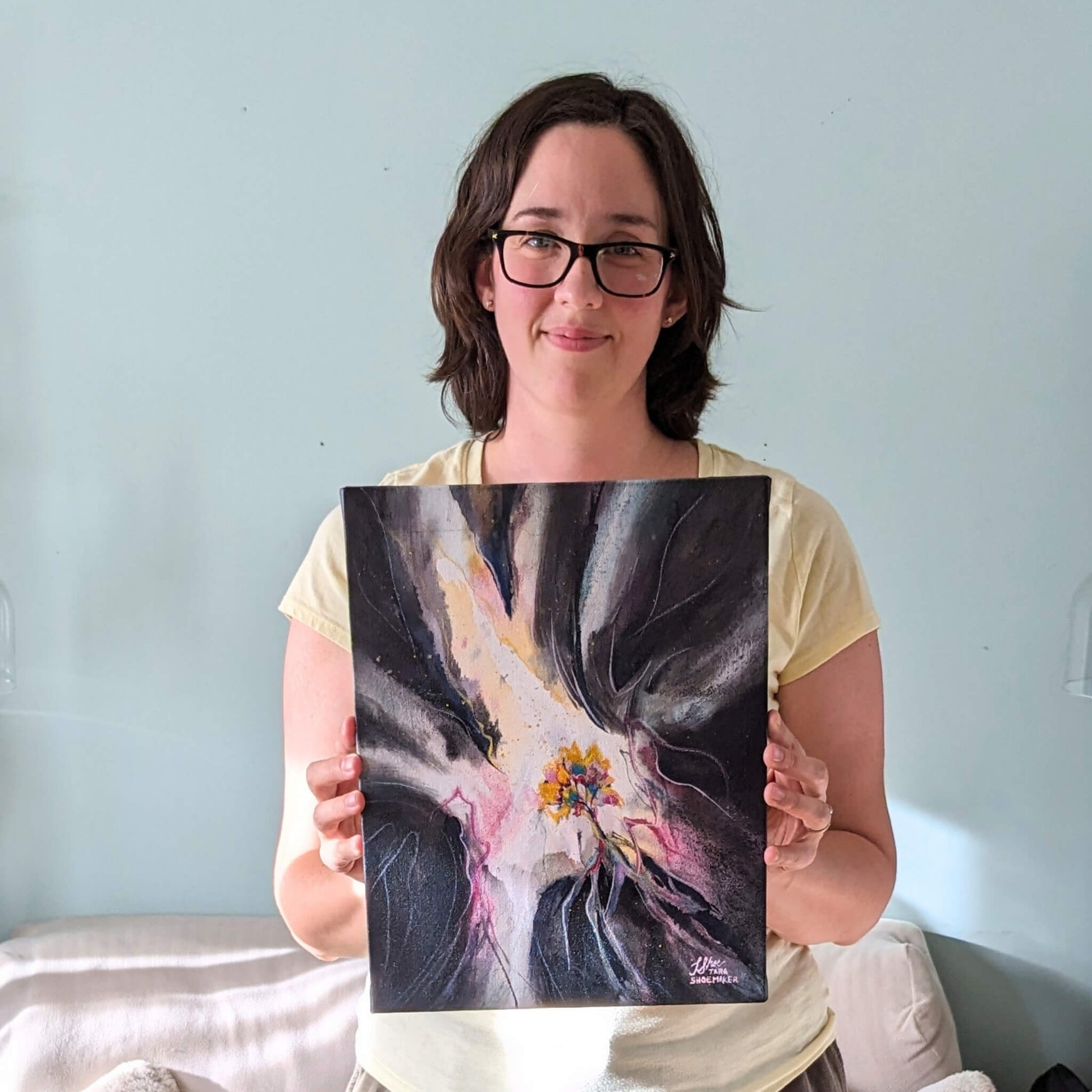 Woman holding a painting against a light blue wall
