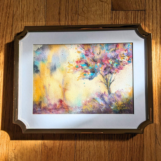 Video zooming in on an abstract tree watercolor painting on a wooden surface.